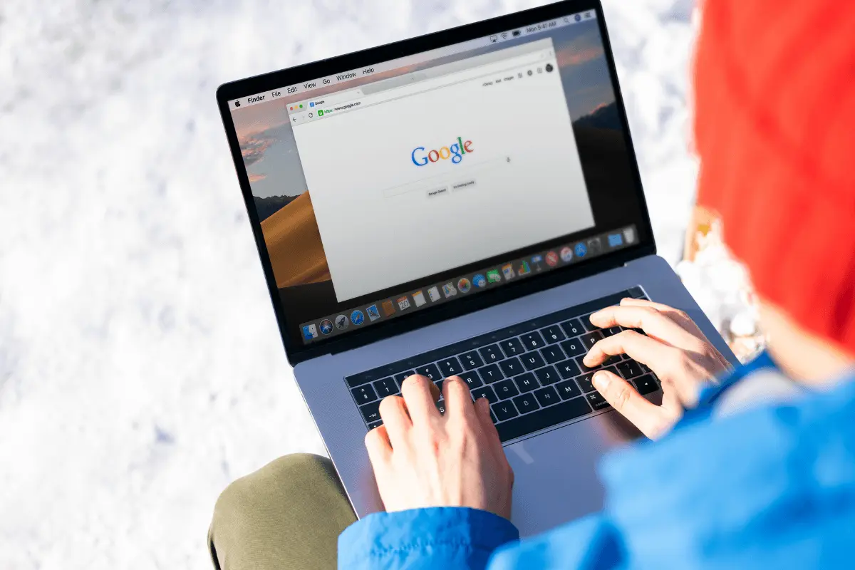 Person using a MacBook laptop with Google search homepage open, sitting outdoors in snowy