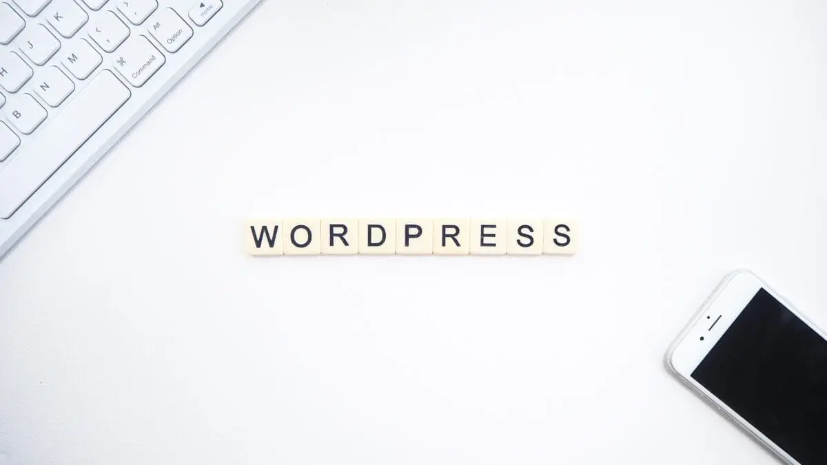 Scrabble tiles spelling "WordPress" on a white background with a keyboard and smartphone in the