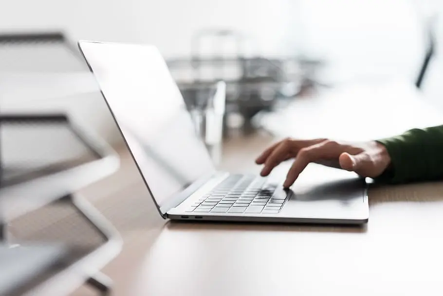 Close-up of a person’s hand typing on a laptop in a bright, modern office setting.