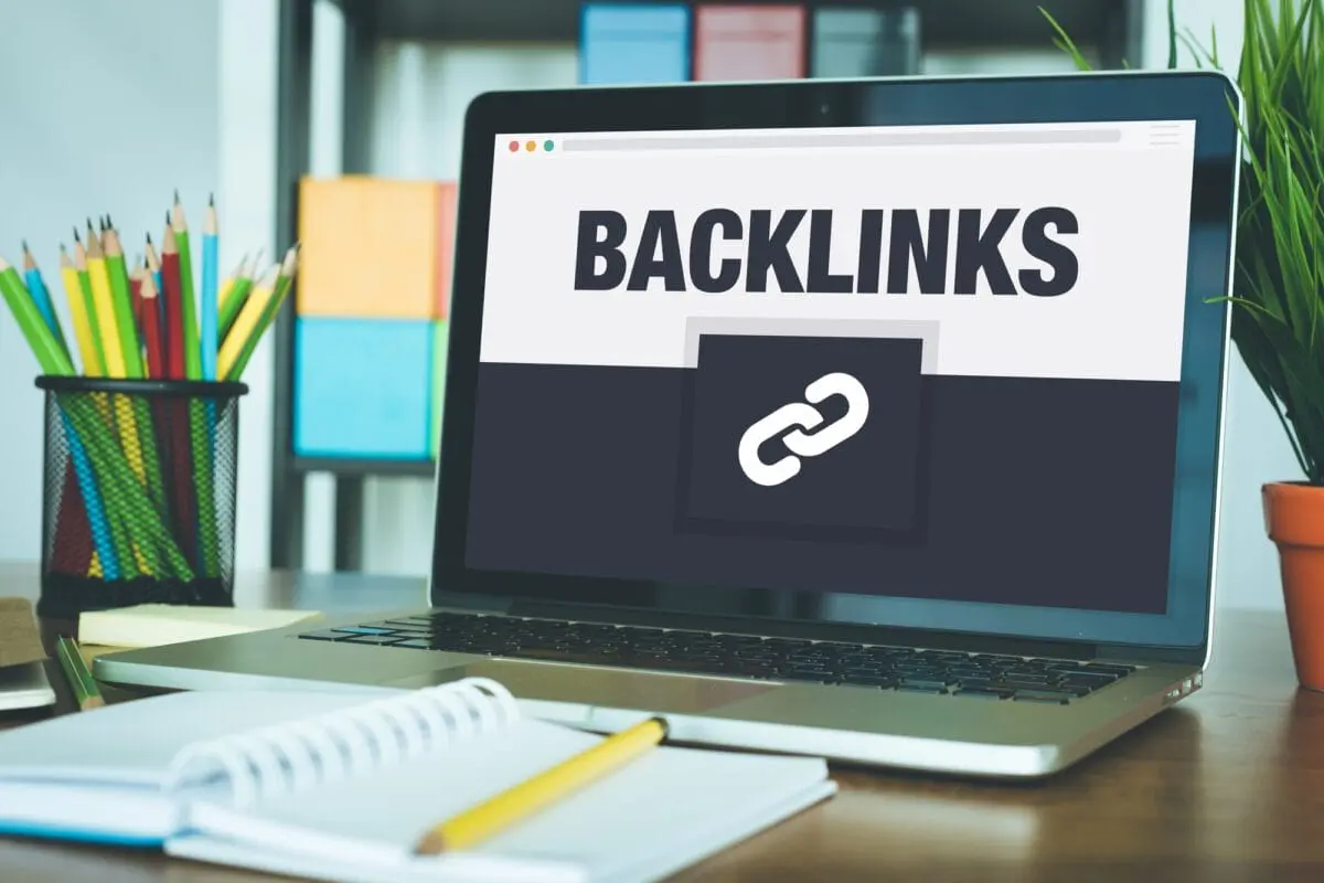 Laptop screen displaying the word "Backlinks" with a link icon, placed on a desk with pencils