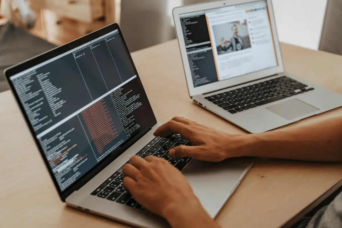 A person working on one laptop that displays code, while another laptop is standing open beside the
