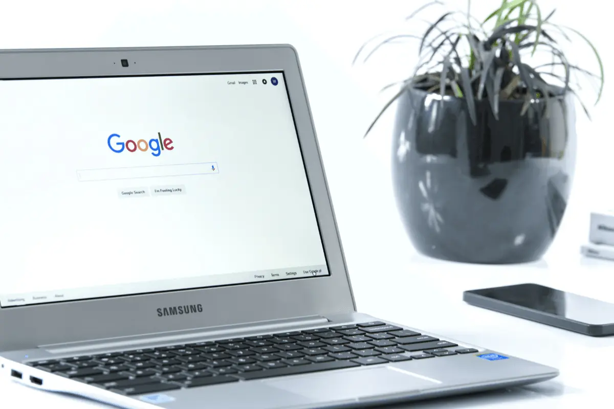Samsung laptop displaying Google search homepage on desk with smartphone and potted plant